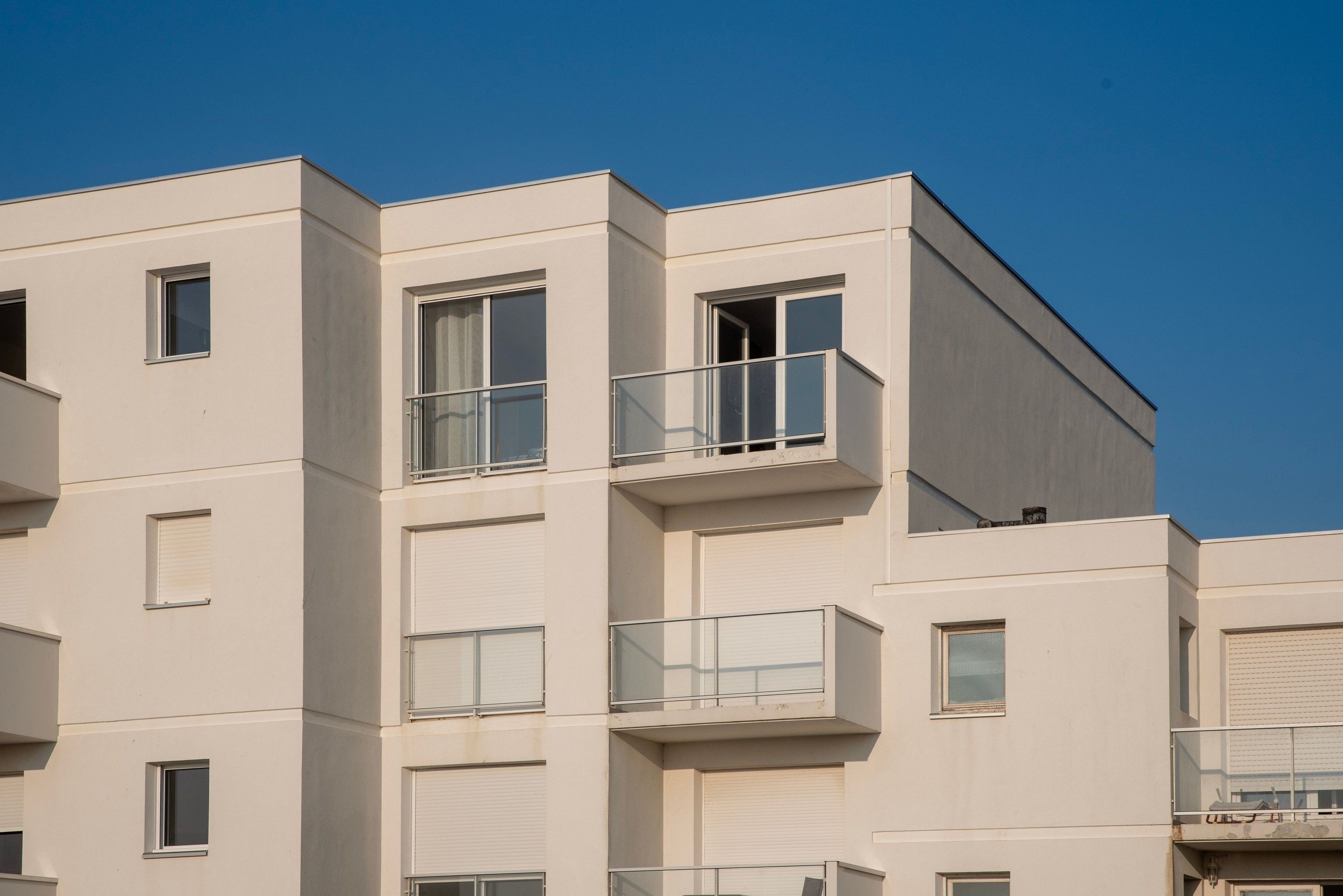 Krem sıvalı apartman cephesinde sürme balkon kapıları ve cam korkuluklar