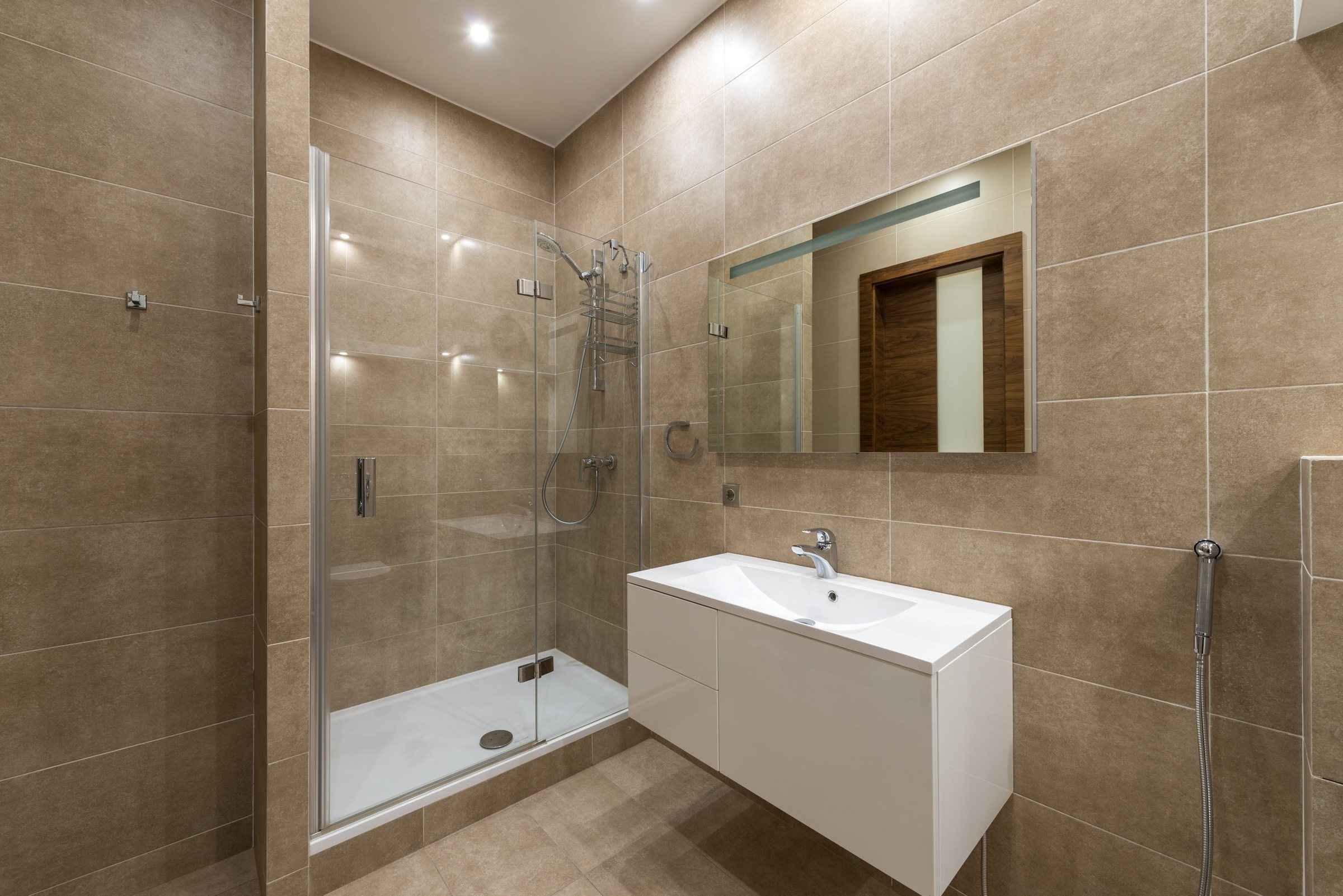 Bej fayanslı banyoda menteşeli cam kapılı duşakabin ve lavabo dolabı